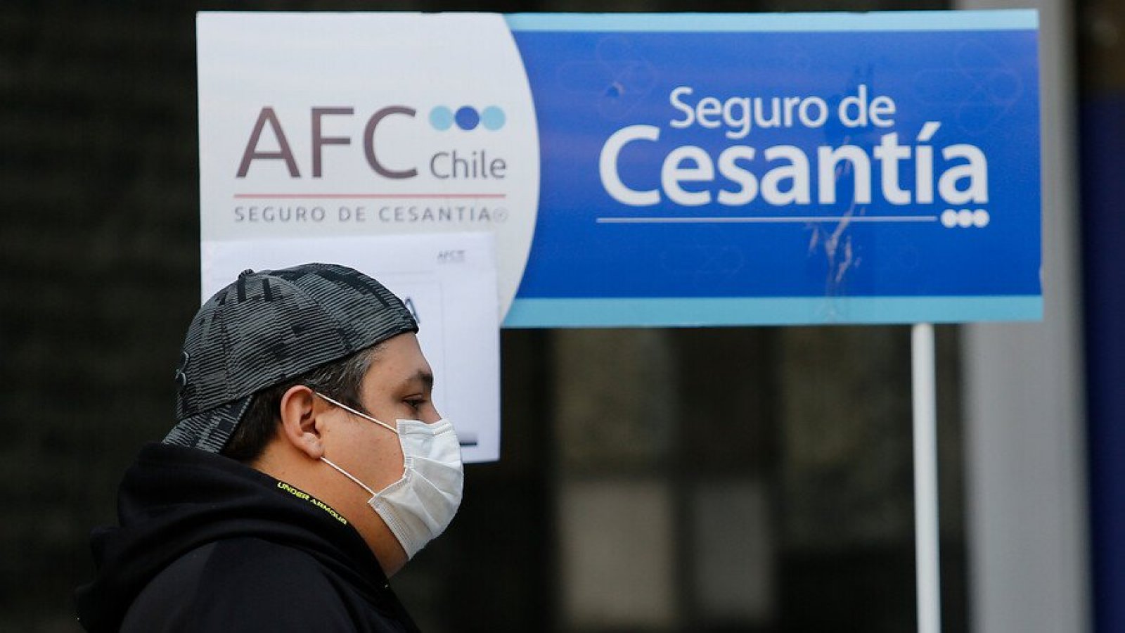 Persona caminando frente un cartel del Seguro de Cesantía de la AFC