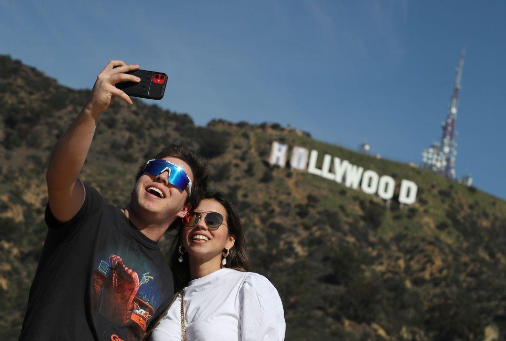 Los turistas Andreas Minniti, izquierda, y su hermana María Pino, derecha, se toman selfies con el letrero de Hollywood el lunes 14 de febrero de 2022 en Hollywood, CA.