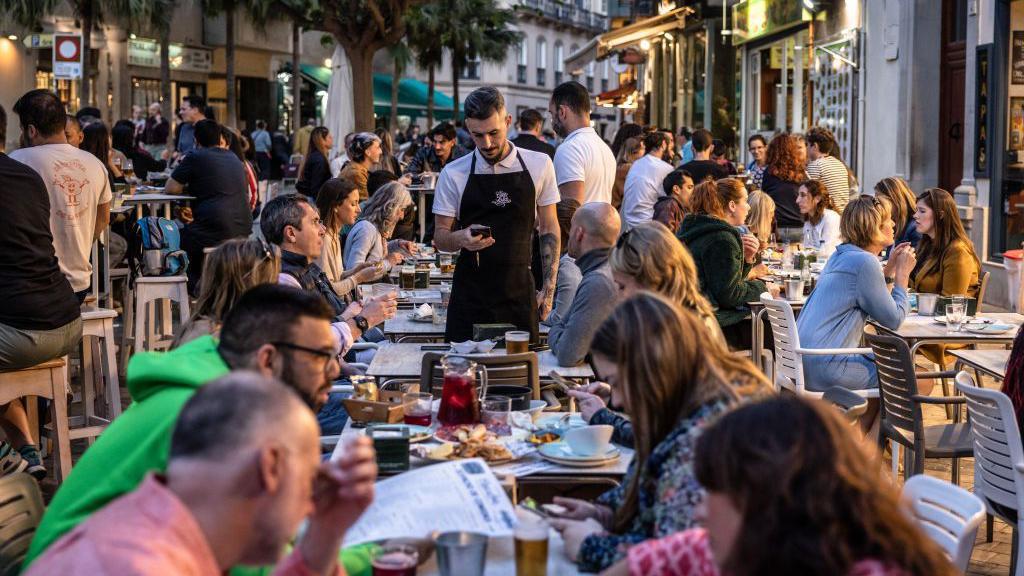 Un camarero atiende a los clientes en una terraza.