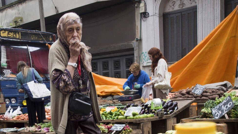 Anciana recorre una feria callejera de frutas y verduras en Montevideo.