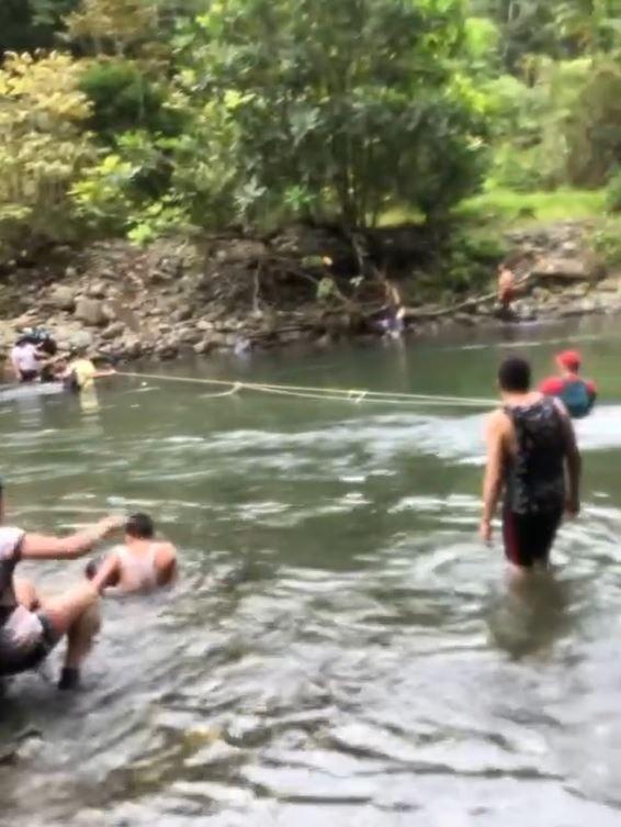 Gente cruzando un río agarrados a una cuerda. 