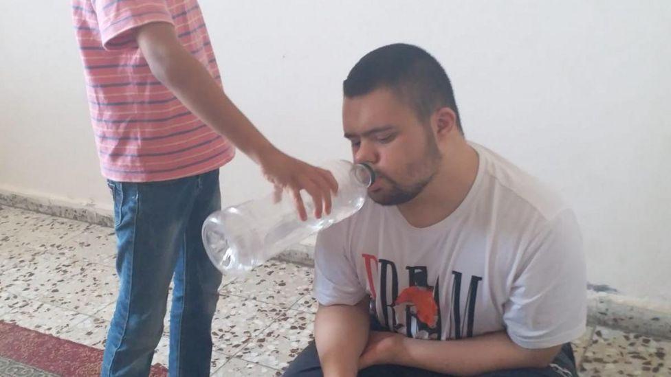 Un niño dando de beber agua a Muhammed con una botella de plástico