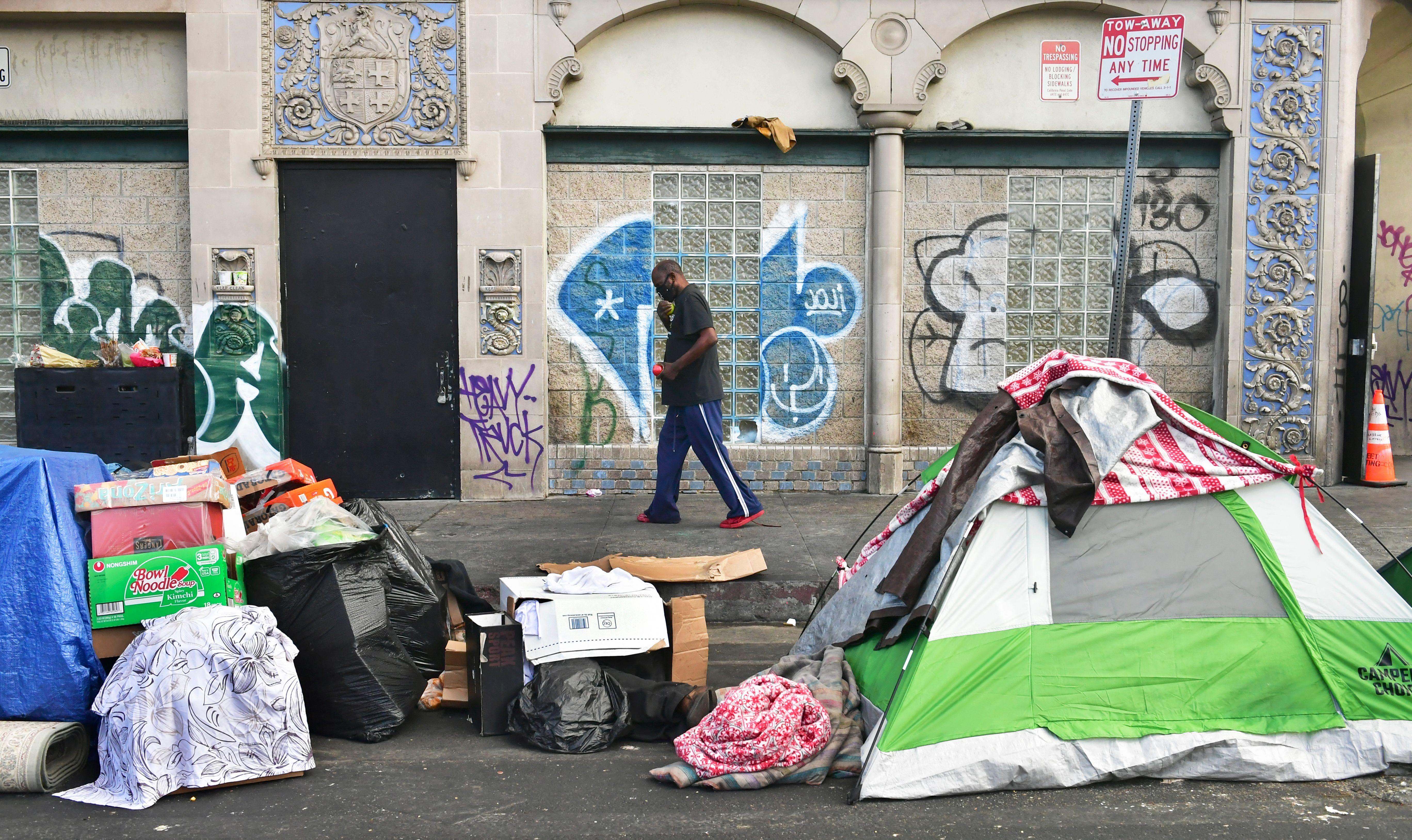 Una persona pasa frente a una carpa de personas sin hogar en la calle. 