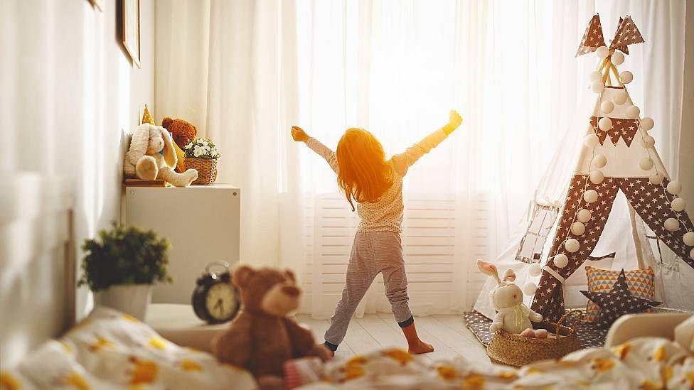 Niña desperezándose frente a una ventana