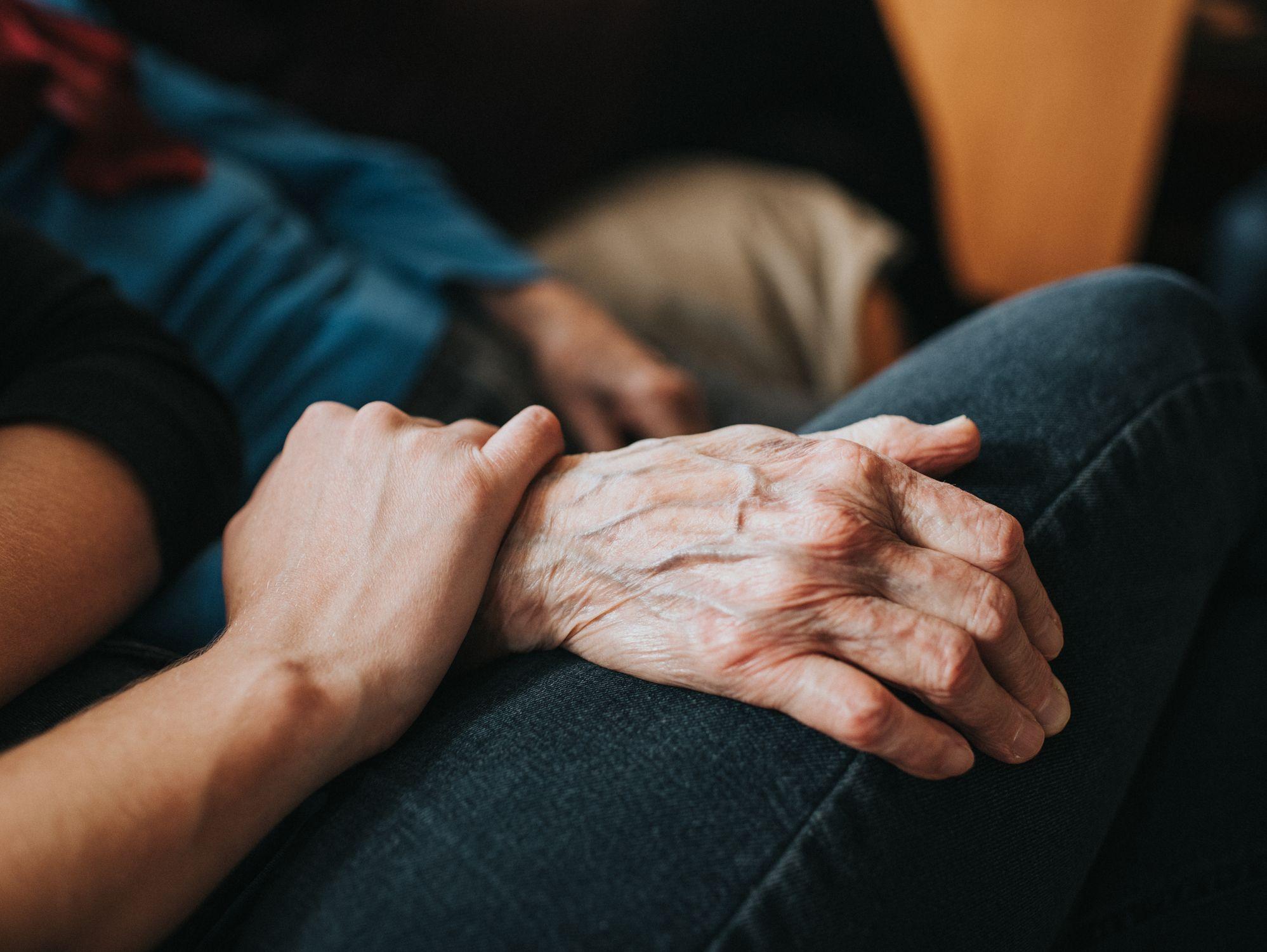 Joven sostiene la mano de un anciano. 