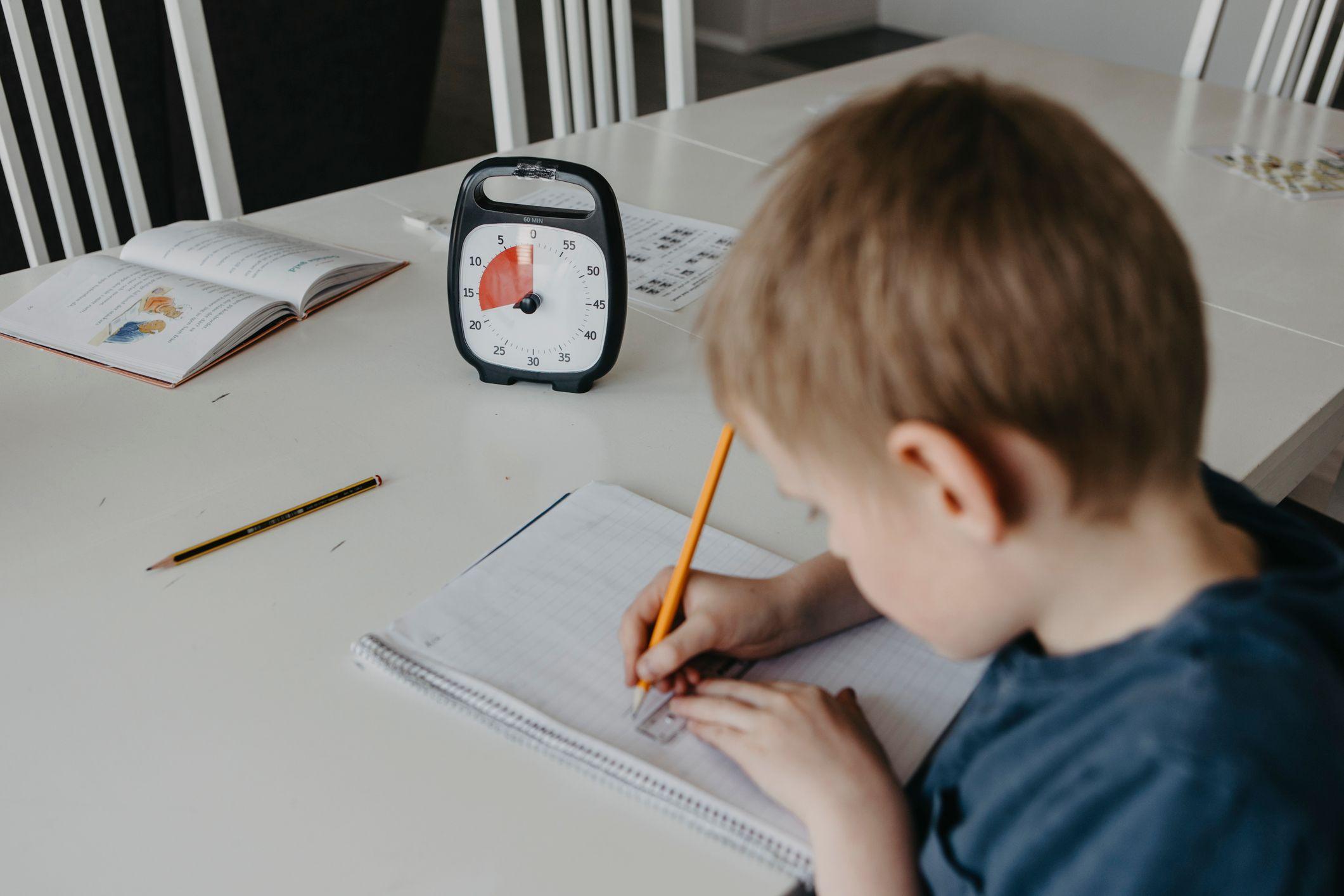 Niños escribe en un papel con un reloj al lado. 