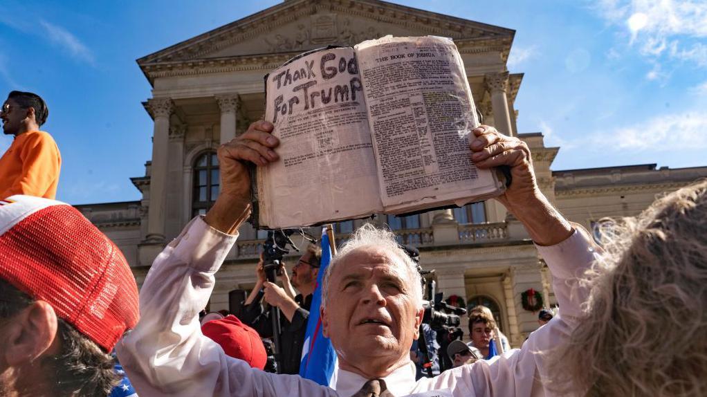 Un manifestante sostiene una Biblia que dice "Gracias a Dios por Trump"  frente al Capitolio del estado de Georgia en noviembre de 2020. 