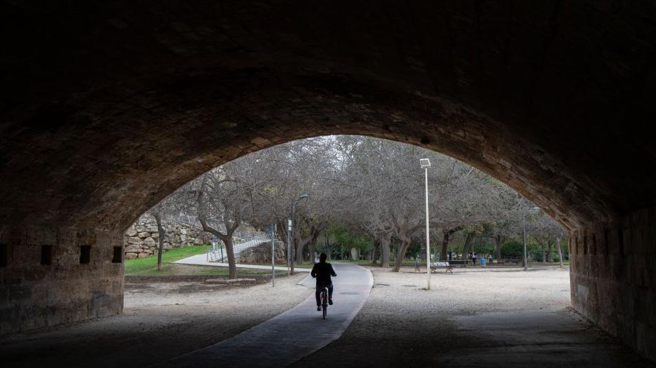 Un señor pasa en bicicleta por debajo de un puente en Valencia.