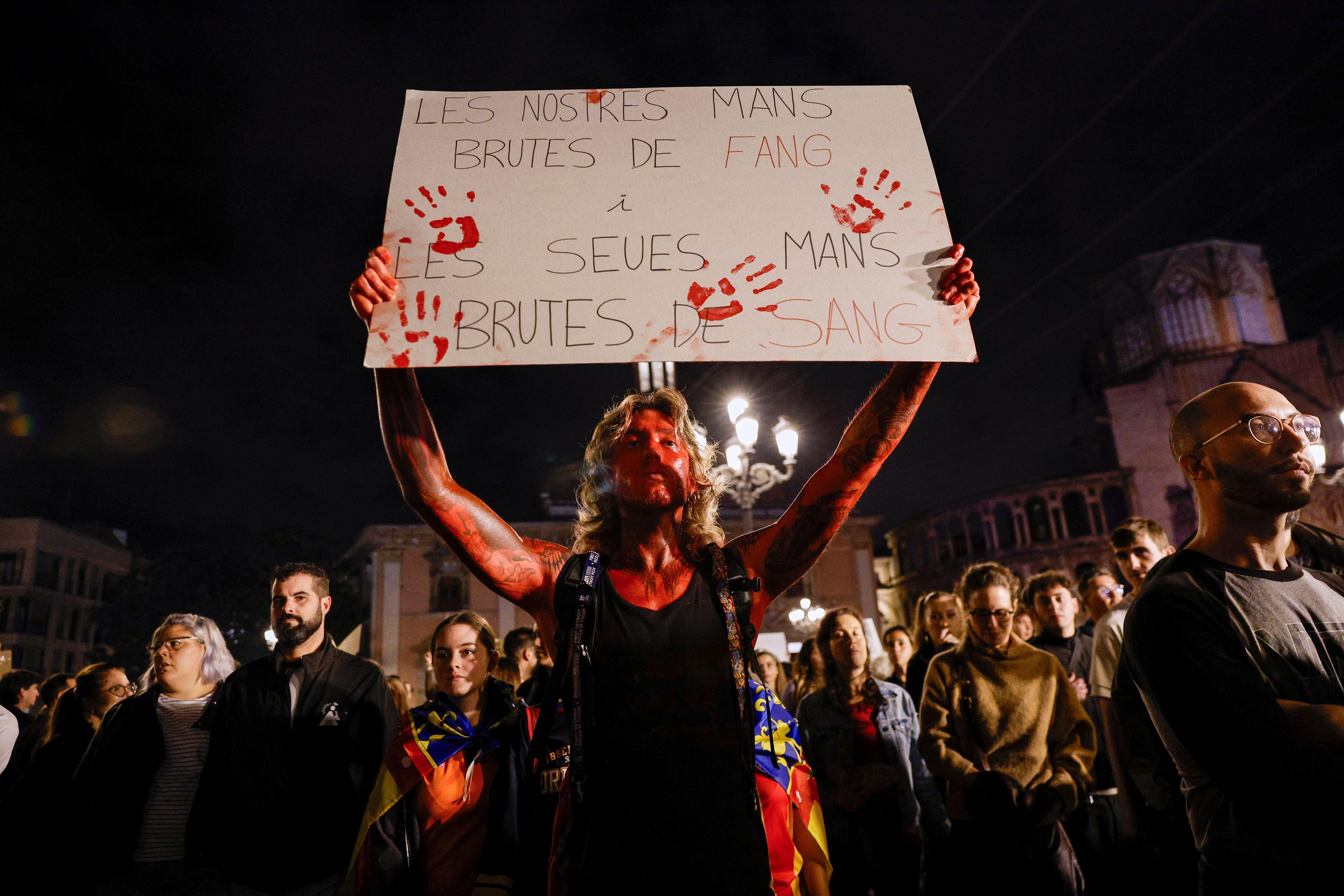 Una persona con pintura roja en el cuerpo carga una pancarta que lee: "Nuestras manos manchadas de barro, las suyas de sangre". 