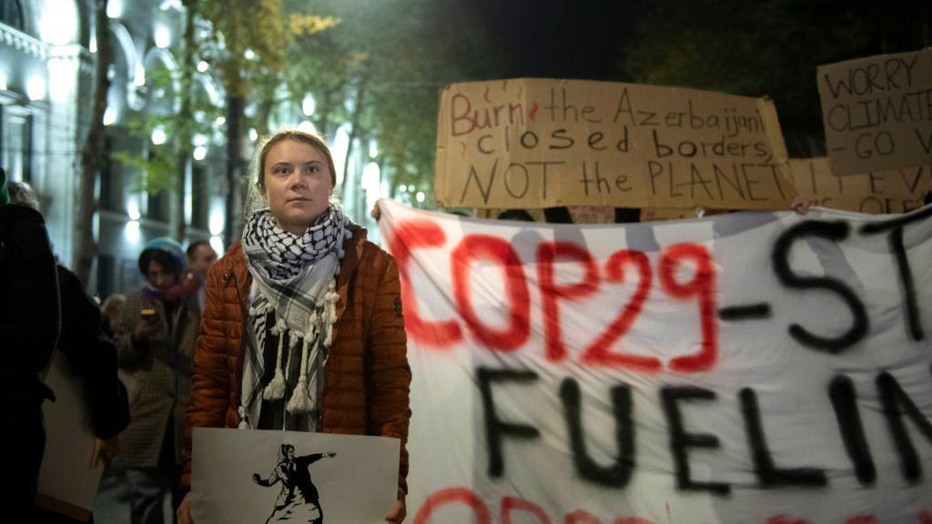 Greta Thunberg en una protesta en Georgia junto a una pancarta que dice "COP29-dejen de alimentar la opresión".