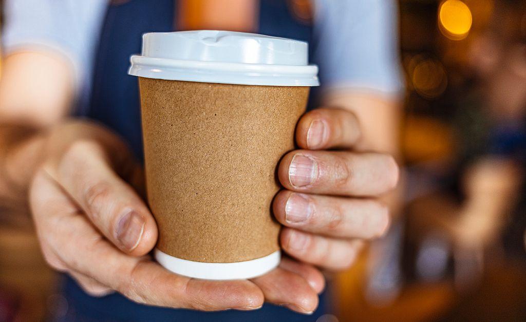 Manos ofreciendo el vaso típico de café o té desechable de las cafeterías. 