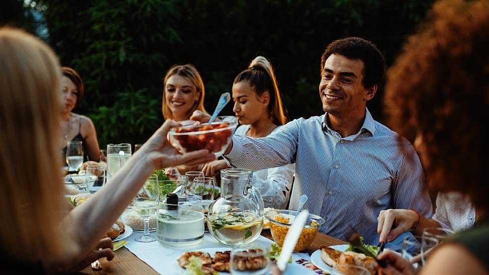 Personas sentadas alrededor de una mesa almorzando al aire libre