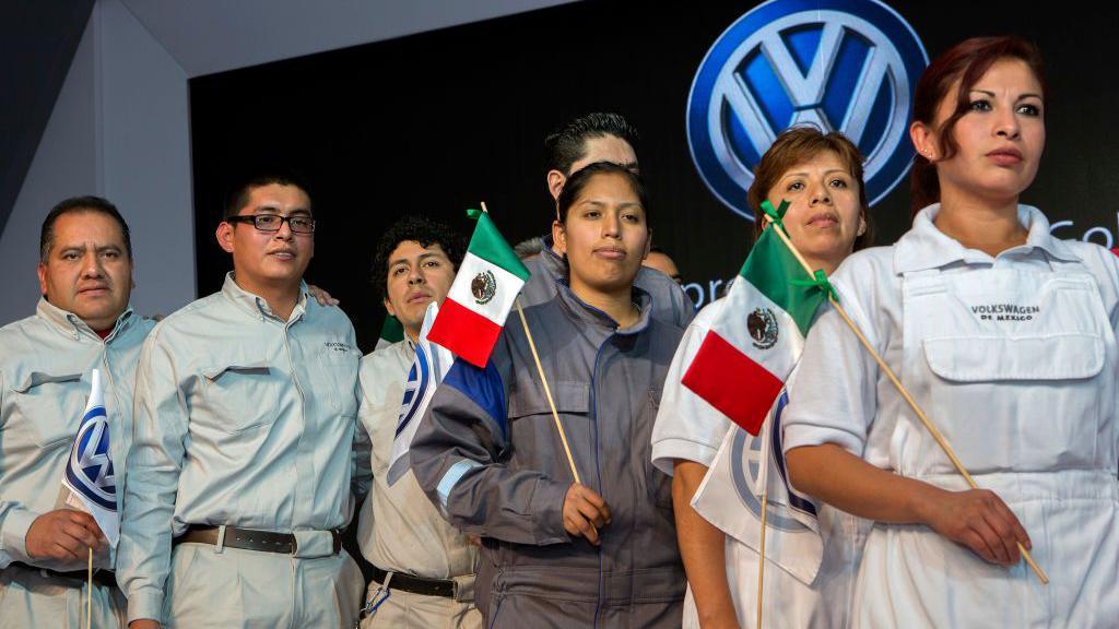 Trabajadores de la planta de VW en Puebla, México, portando la bandera del país bajo el logo de la marca.