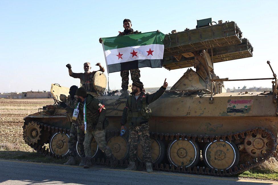 Rebeldes en un vehículo militar con la bandera de Siria