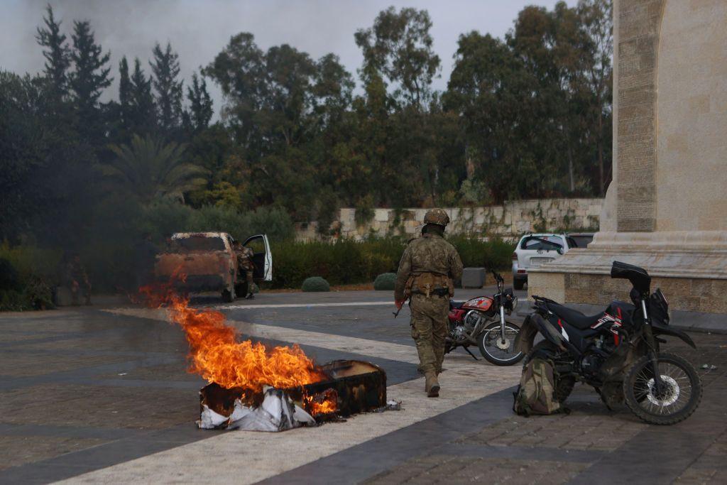 Un combatiente sirio camina junto a un ataúd en llamas fuera del mausoleo de Hafez al Assad.