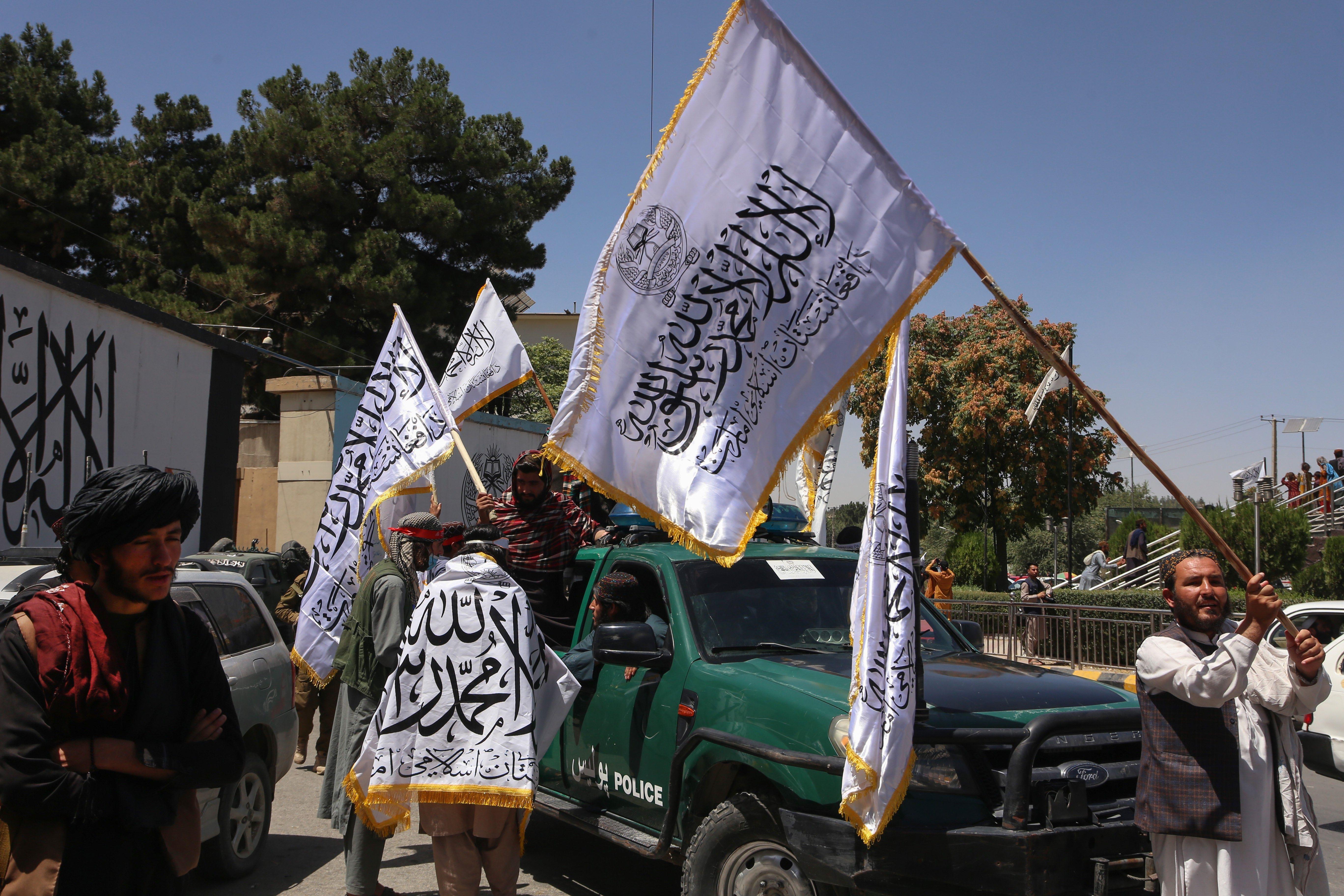 Afganos sostienen banderas para celebrar el segundo aniversario de la toma del poder por los talibanes en Kabul.