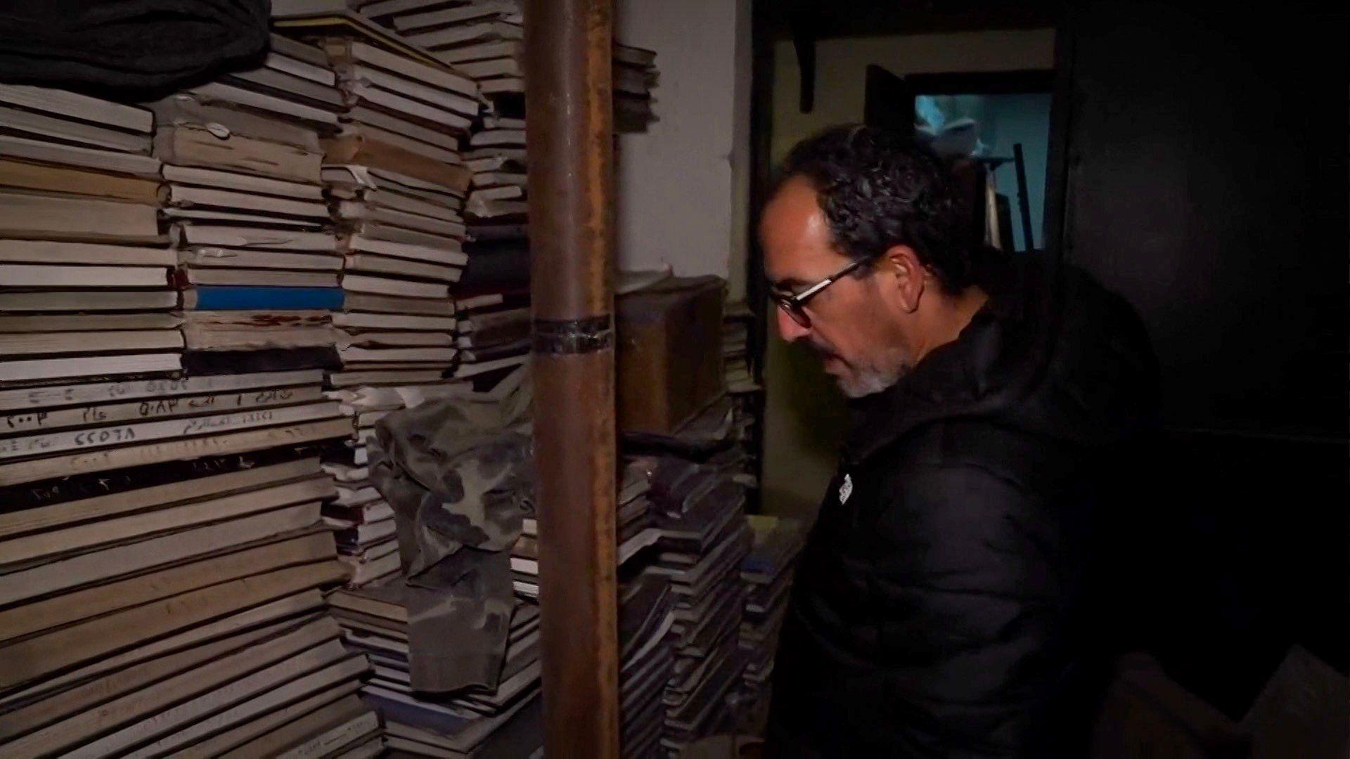 Feras Kilani mira una pila de libros en un cuarto oscuro 