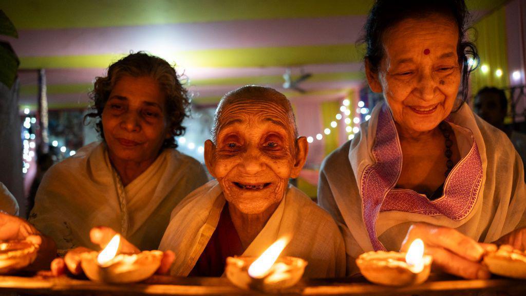 Tres mujeres mayores en el hogar de ancianos Pramod Talukdar Memorial encienden lámparas de aceite Diya mientras celebran Diwali en Guwahati, India, el 1 de noviembre de 2024