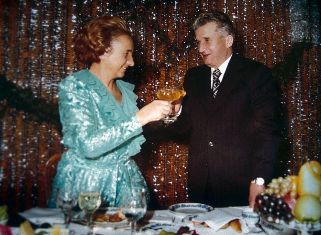 Nicolae Ceausescu y su esposa Elena comparten un brindis, ambos vestidos elegantes, él con traje y corbata, ella con un vestido de tela lujosa y brillante, en una fotografía sin fecha de su álbum familiar.